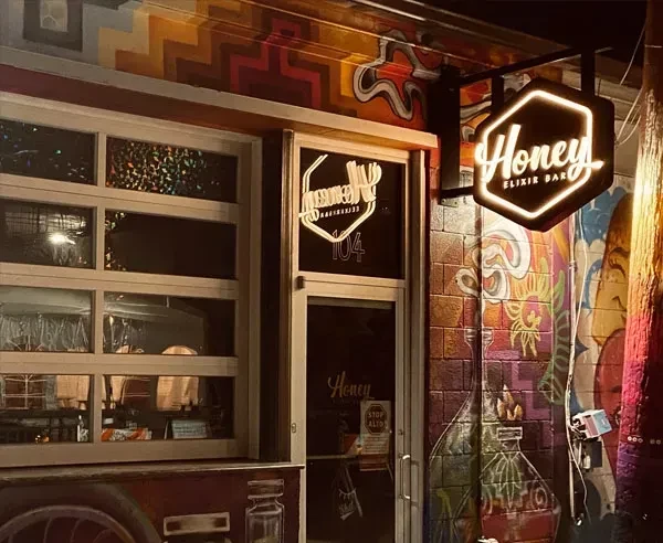 Honey Elixir Bar exterior, murals with lab glassware, and glowing signs.