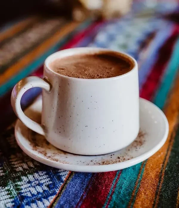 White speckled mug with dark foamy drink on a vibrant patterned fabric.