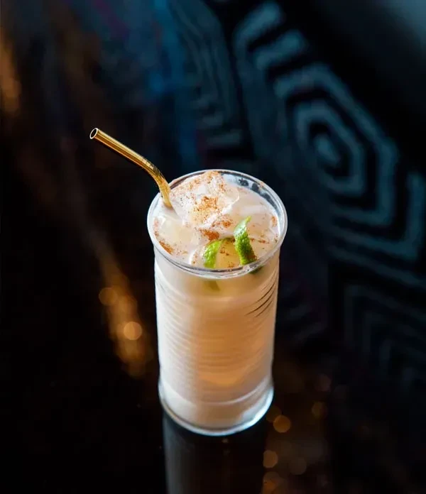 Creamy cocktail in tall ridged glass with lime, spice, and golden straw.