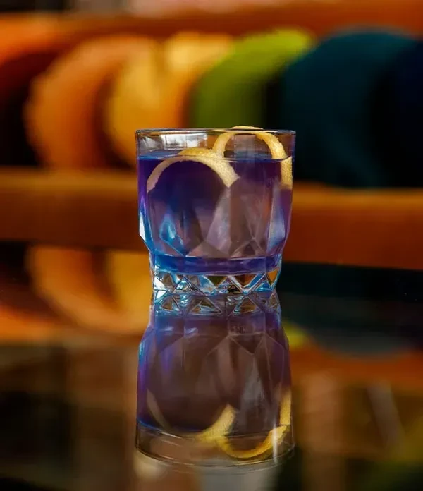 Blue or purple cocktail in faceted glass with twisted citrus peel.