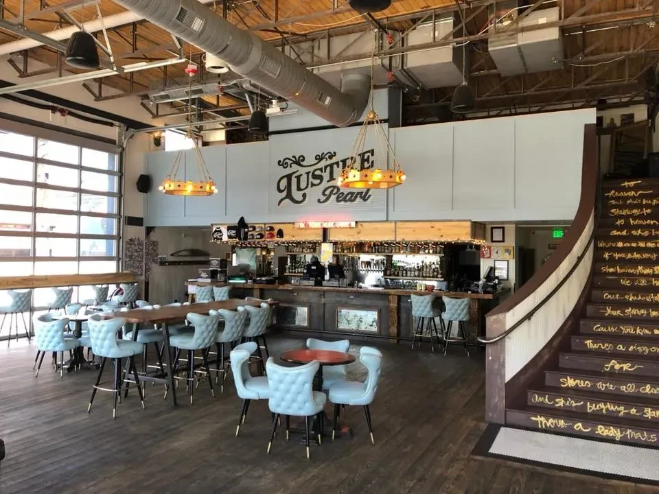 Spacious industrial restaurant interior with bar, seating, and scripted wooden staircase.