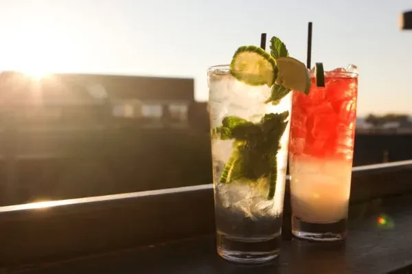 Two drinks, one clear, one layered, against a sunset cityscape.