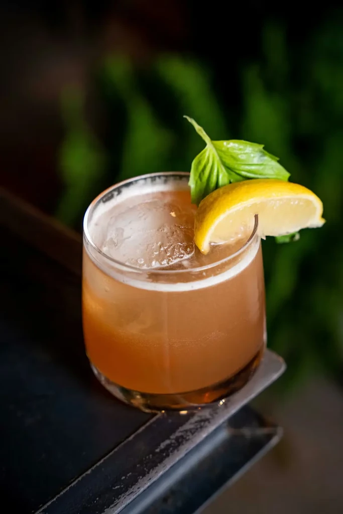 Amber cocktail in a rocks glass with lemon, basil, and ice.
