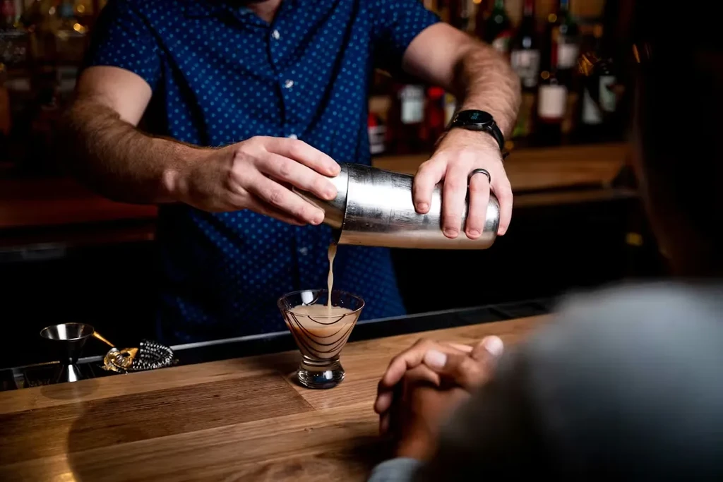 Bartender pouring cocktail from shaker into a stemmed glass.