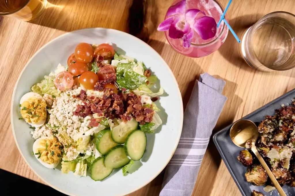 Overhead view: Cobb-style salad, roasted brussels sprouts, pink orchid cocktail.