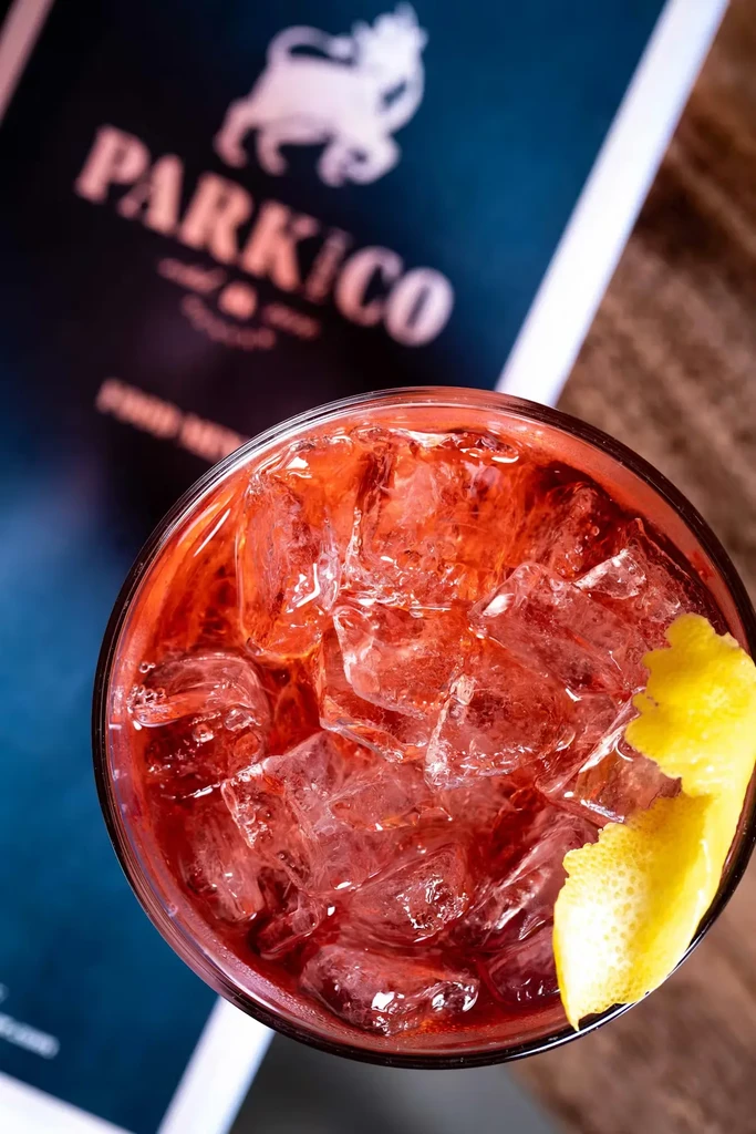 High-angle red cocktail with lemon peel, ice, and PARKICO background.