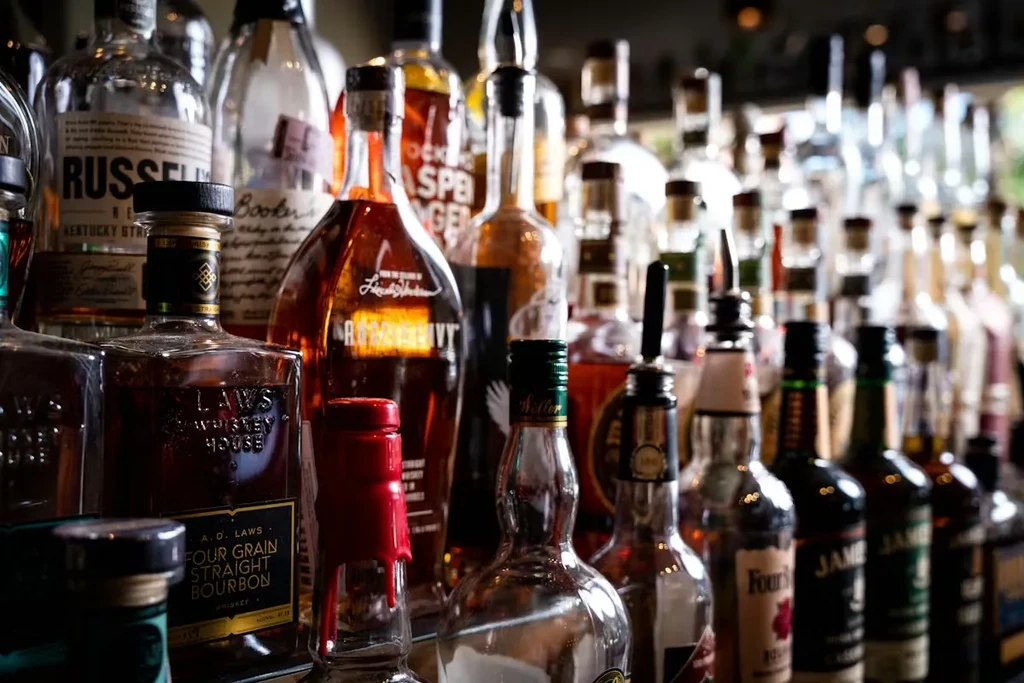 Arranged whiskey and bourbon bottles sharply focused on a bar shelf.
