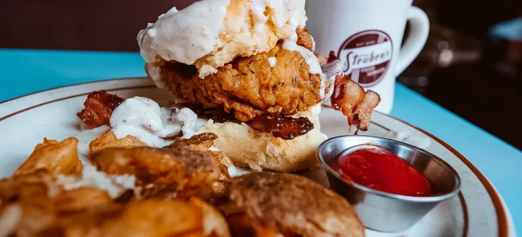 Fried chicken biscuit sandwich, gravy, bacon, potatoes, and ketchup.