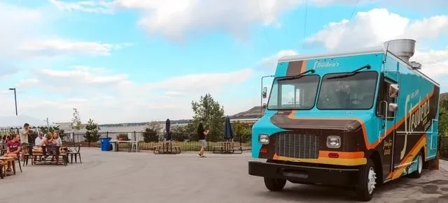 Teal Steeden's food truck, people dining outdoors by a lake.