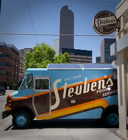 Blue and brown Steuben's food truck with solar panels on sunny city street.