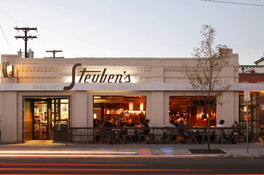 Illuminated Steuben's Food Service restaurant exterior with patrons dining at dusk.