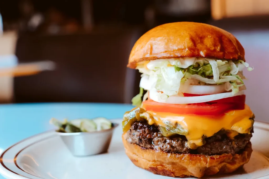 Stacked cheeseburger with melted cheese, tomato, onion, and a side of pickles.