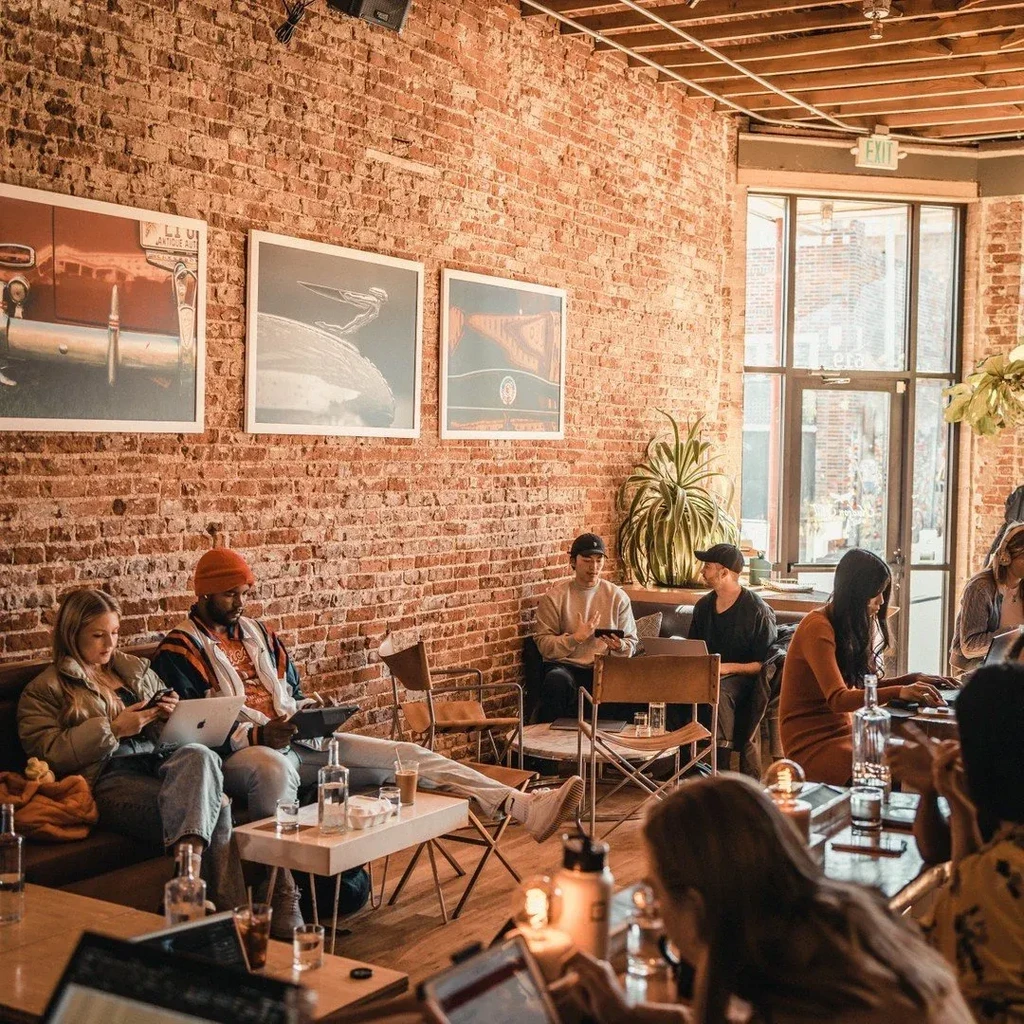Industrial-chic cafe with brick, beams, people on laptops, warm light.