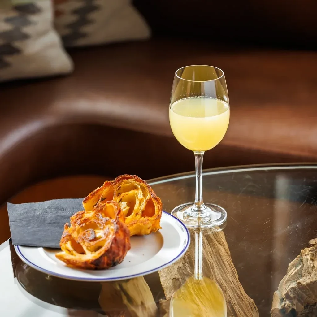 Close-up: stemmed glass with pale drink, two golden flaky pastries.