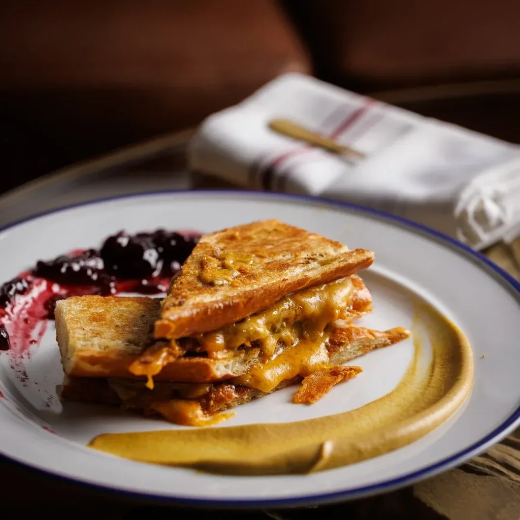 Golden toasted sandwich with melted cheese, berry jam, and mustard.
