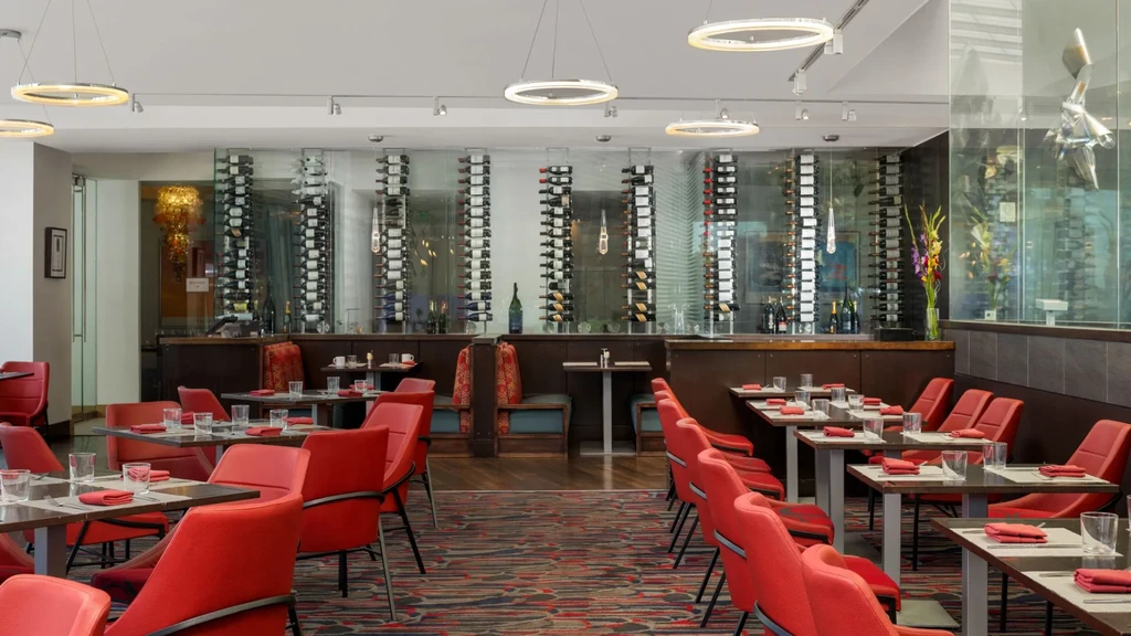 Empty modern restaurant dining room with red chairs and wine display.