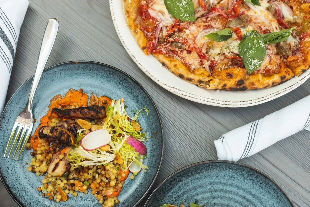 Overhead: rustic pizza and pasta with grilled protein and fresh salad.