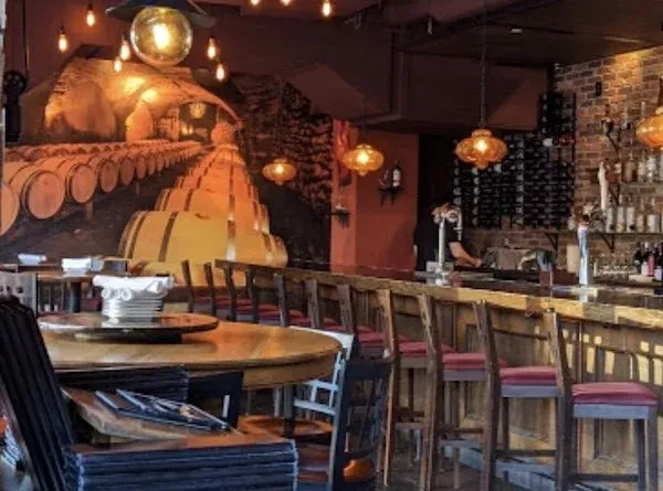 Warm restaurant interior with a bar, wooden tables, and barrel mural.