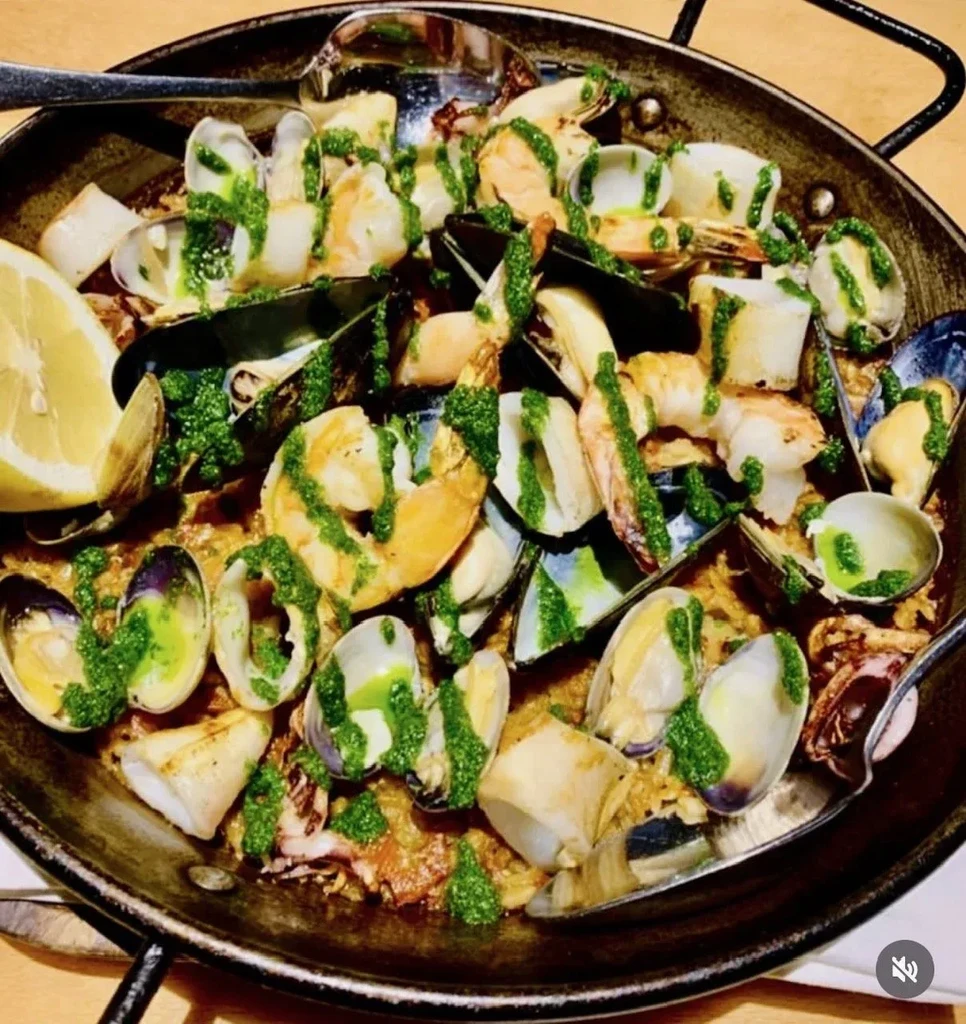 Pan of seafood paella with mussels, green sauce, and lemon.