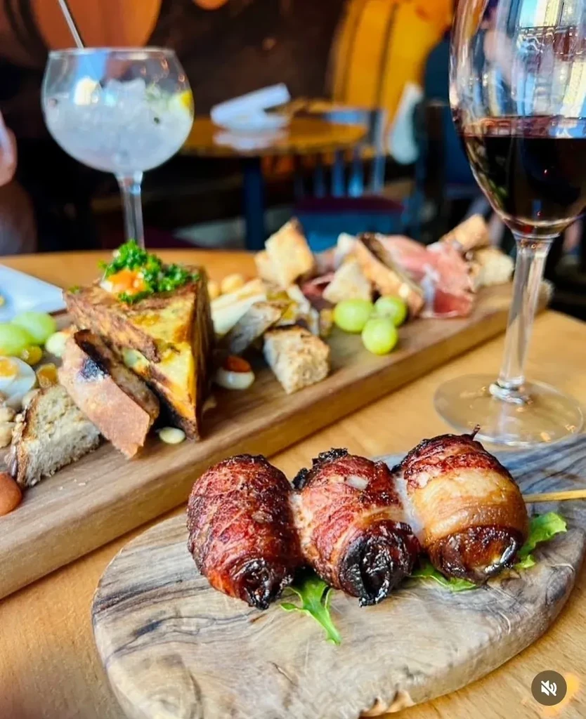 Warm close-up of bacon appetizers, Spanish tortilla, cured meats, and drinks.