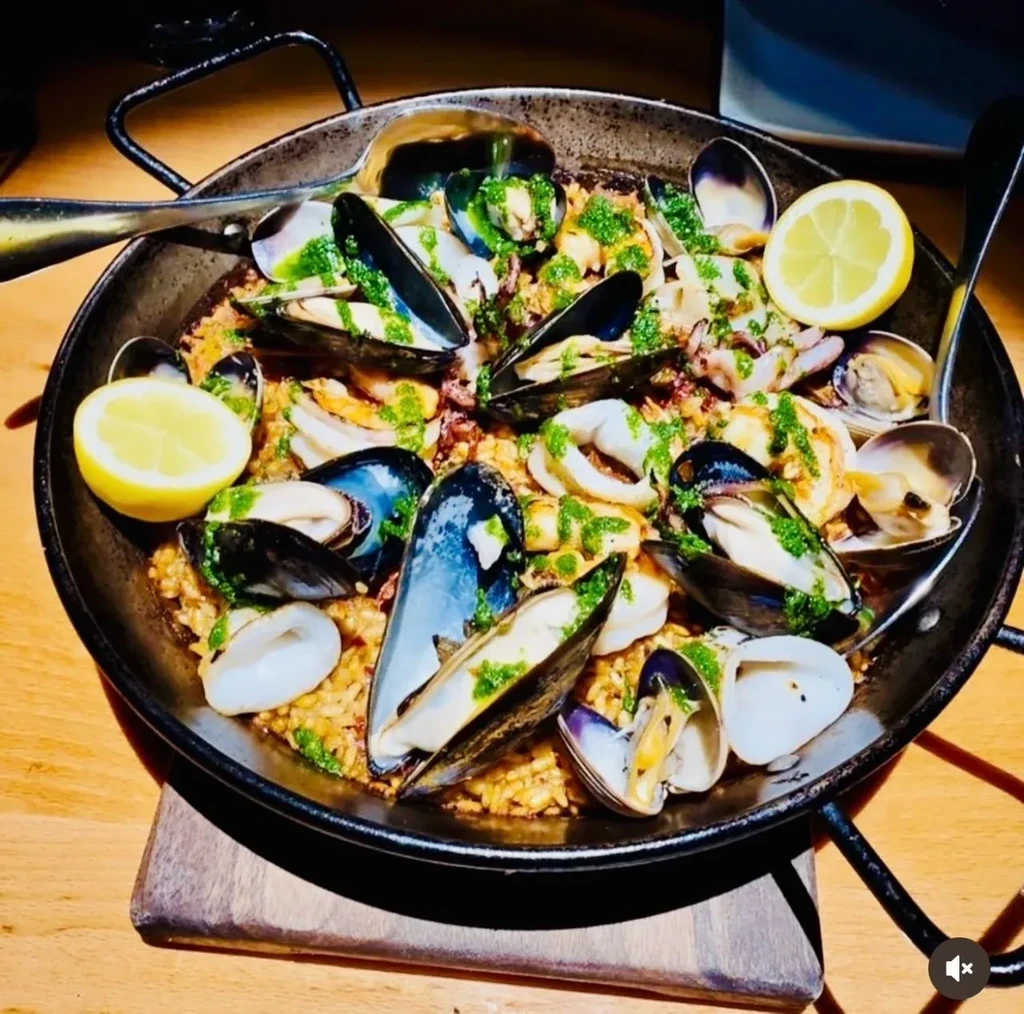 Seafood paella in pan with mussels, clams, green sauce, and lemon.