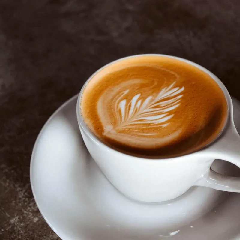 White cup of latte with intricate leaf latte art.