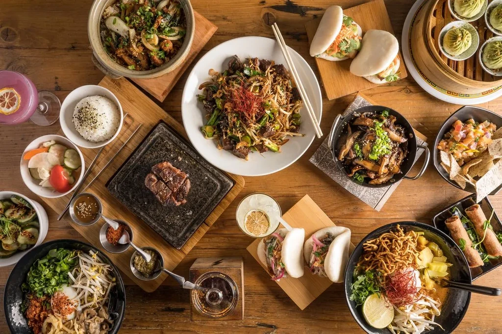 Overhead shot of diverse Asian cuisine and drinks on a rustic table.