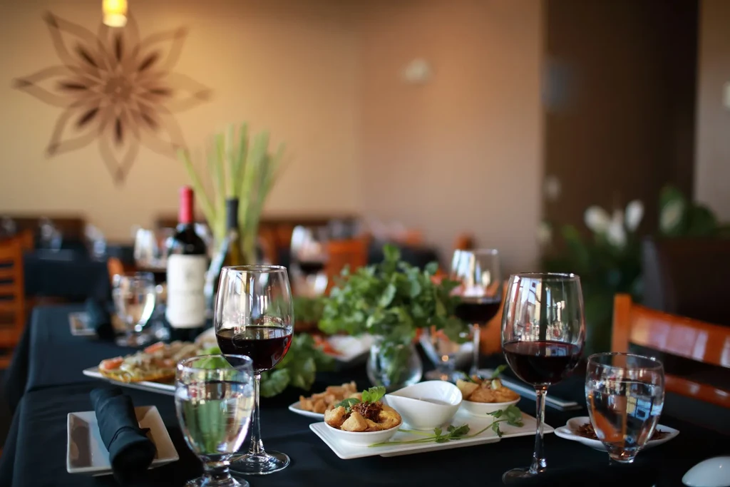 Black tablecloth set with red wine, water, and small garnished appetizers.