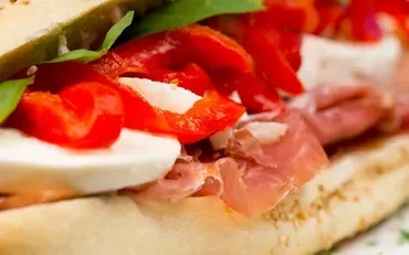Ham, mozzarella, roasted peppers, and leafy greens sandwich cross-section.