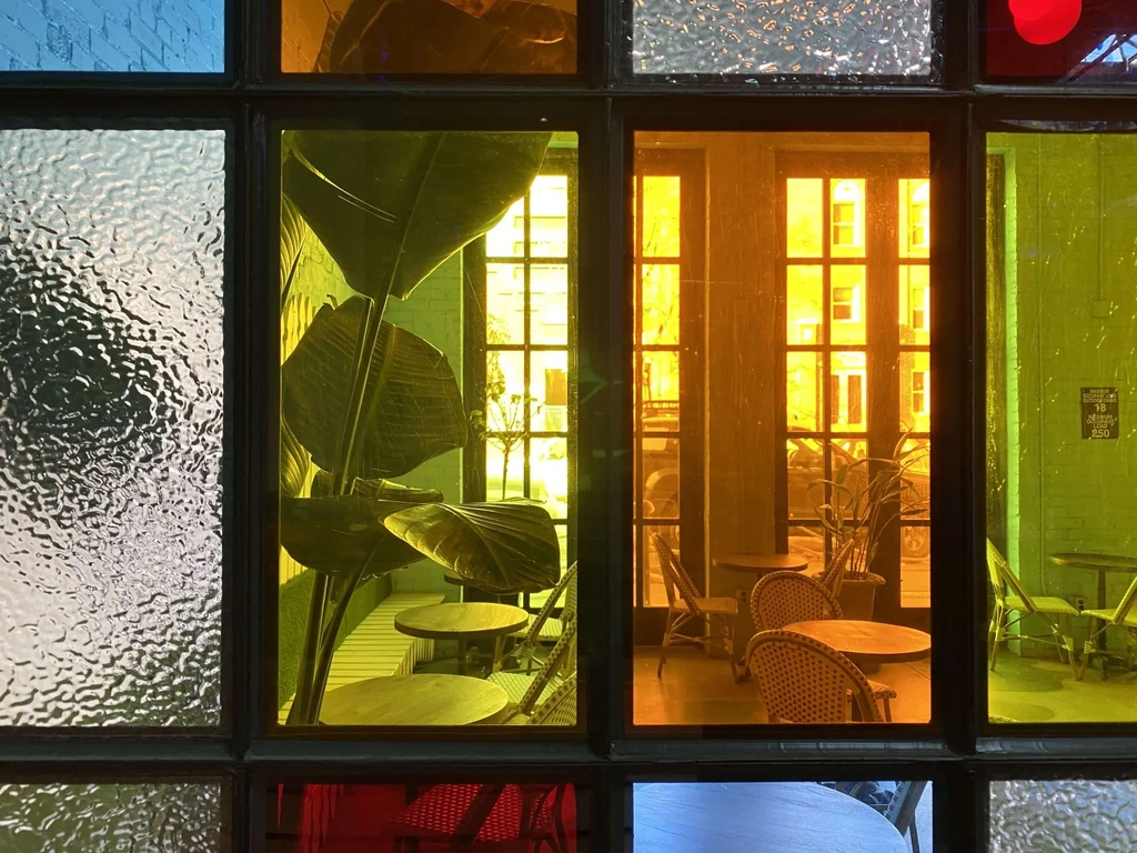Plant-filled restaurant interior viewed through a vibrant stained-glass window.