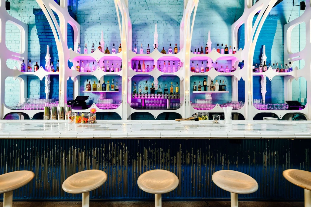 White bar counter, arched shelves, and purple-lit liquor bottles.