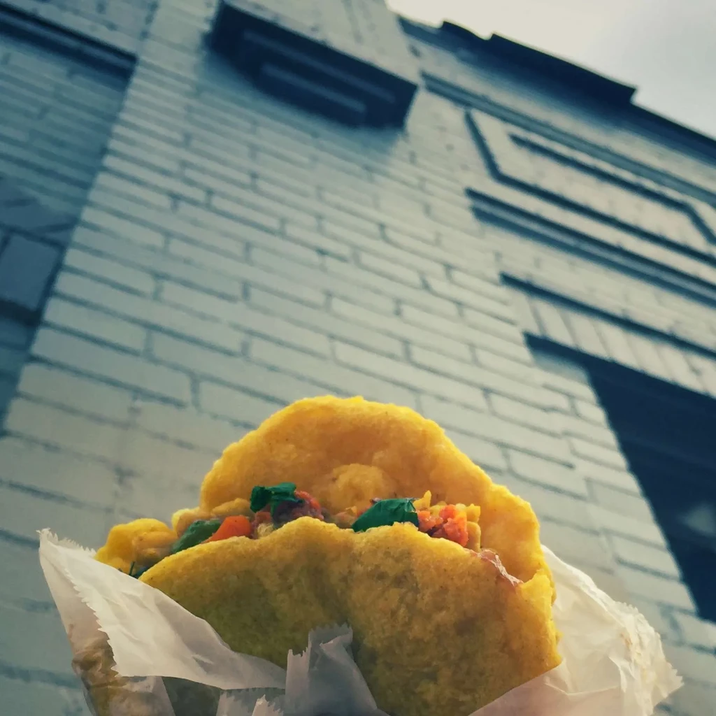 Handheld fried dough pocket with colorful filling, partially wrapped in paper.