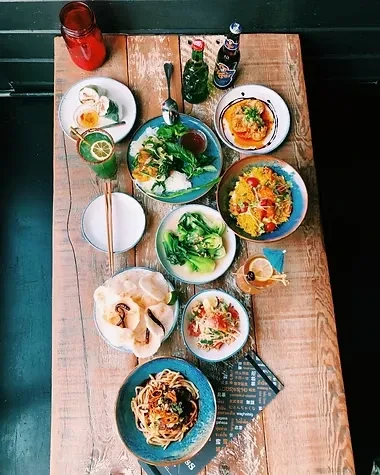 Rustic wooden table laden with diverse, colorful Asian dishes and drinks.