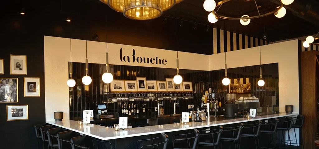 La Bouche's modern bar features a white counter and black tile backdrop.