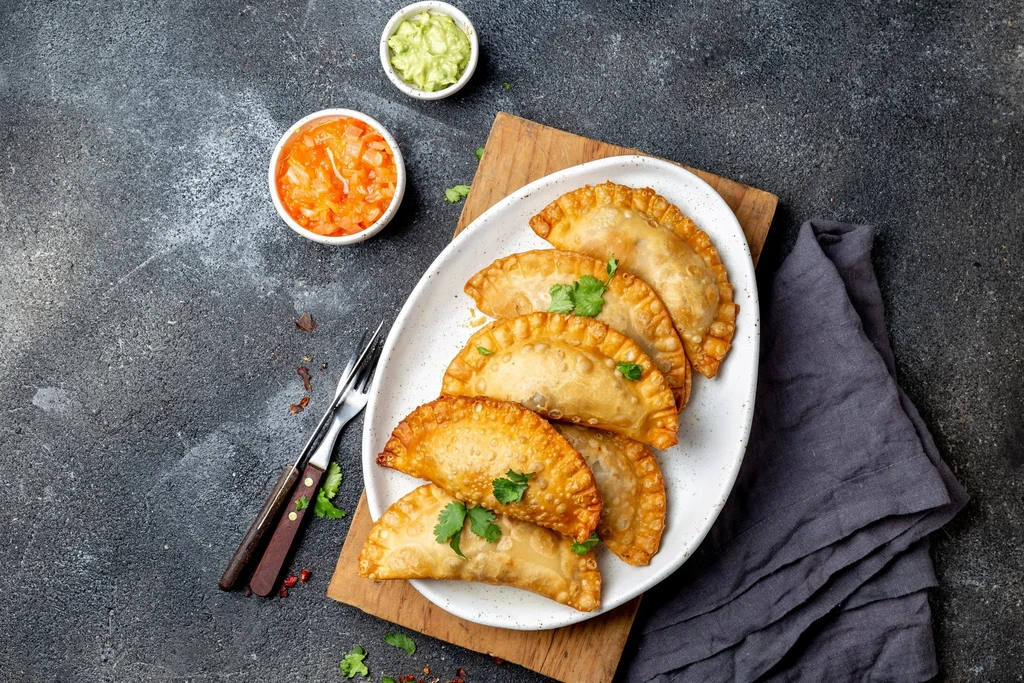 Six golden-brown empanadas garnished with cilantro, served with salsa and guacamole.