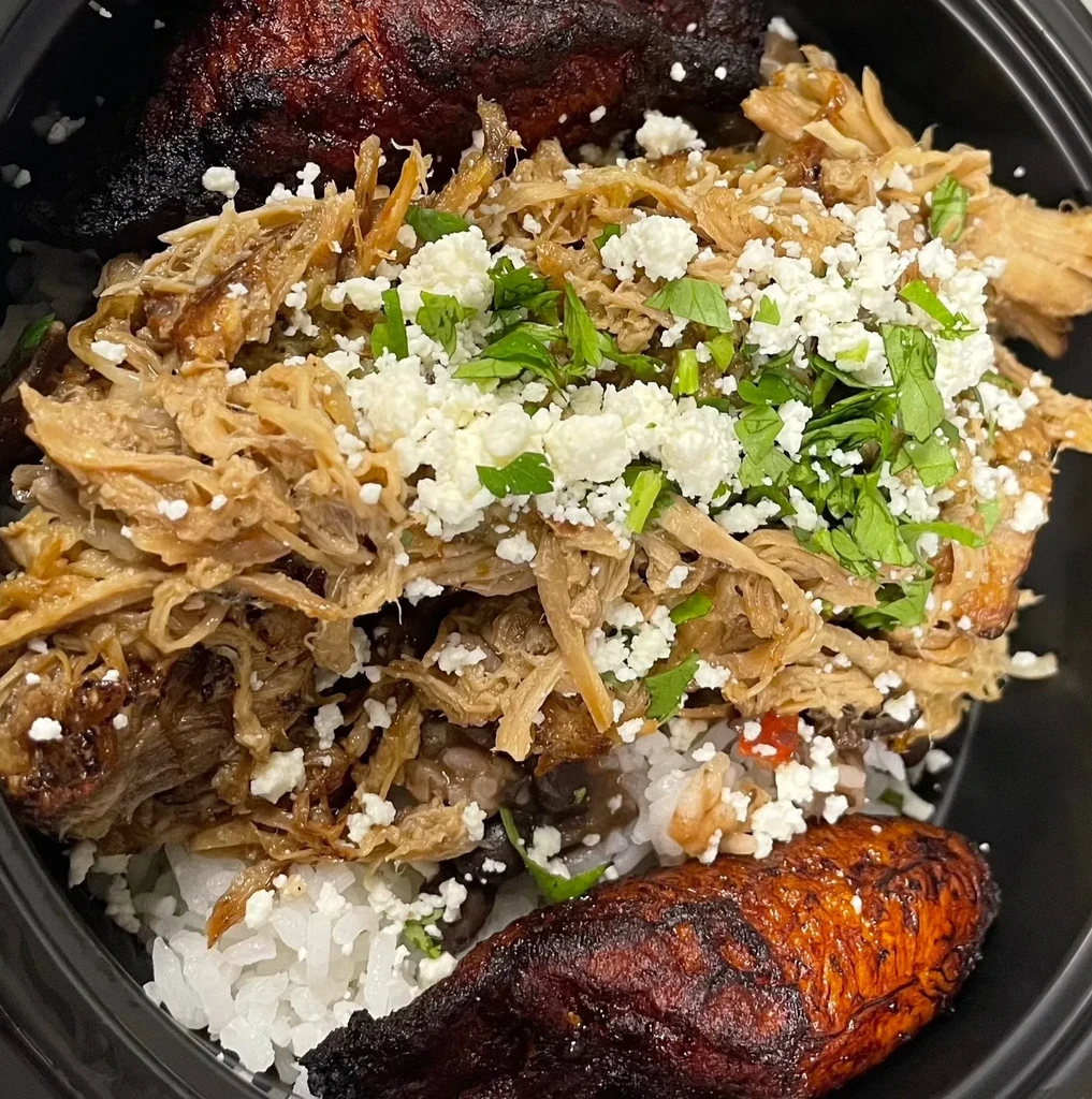 Shredded pork, rice, beans, cheese, herbs, and fried plantains in a bowl.