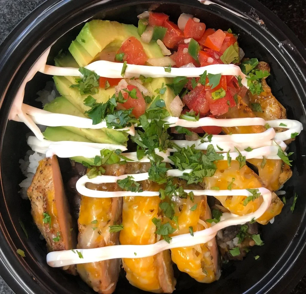 Colorful layered bowl with avocado, pico de gallo, protein, rice, and beans.