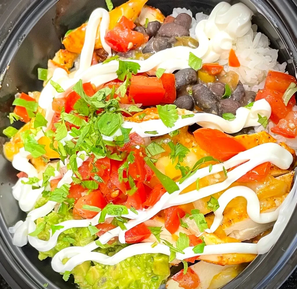 Colorful chicken burrito bowl with rice, beans, avocado, and crema.
