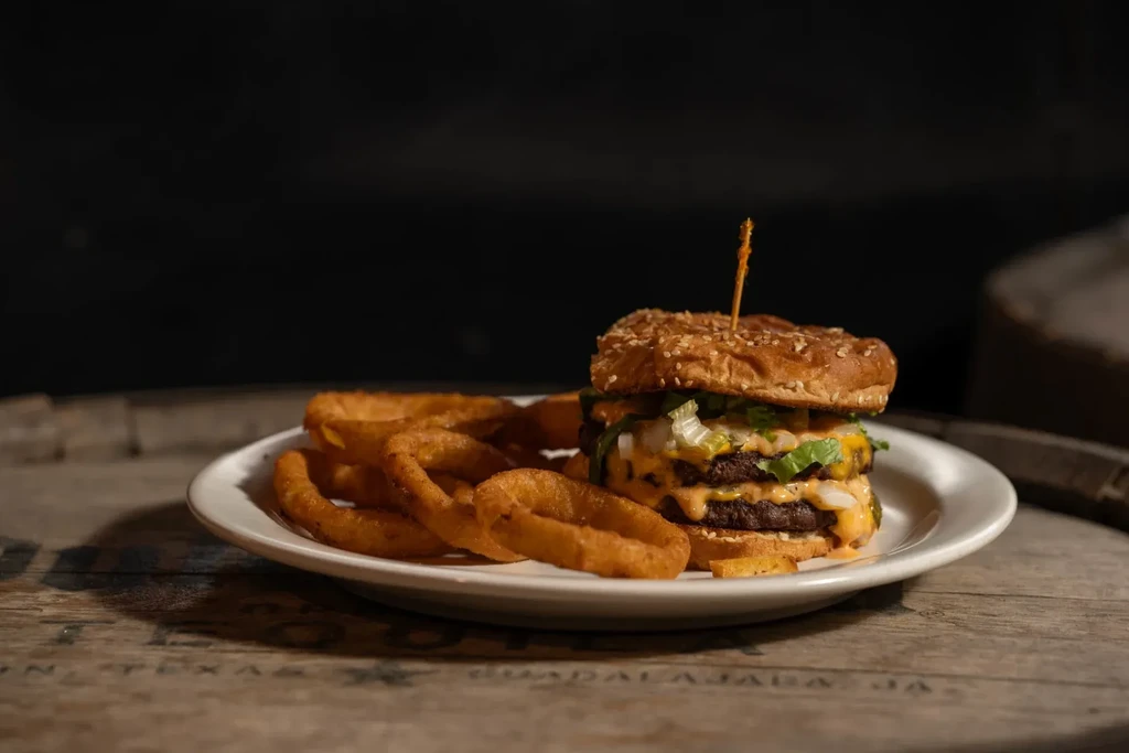 Double-patty burger with cheese, lettuce, and onion rings on wood.