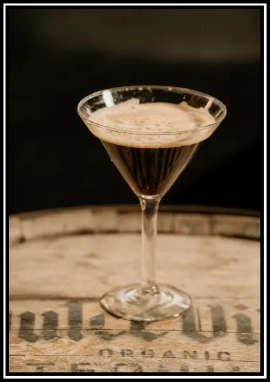 Dark brown foamy martini cocktail on a wooden surface with "ORGANIC".