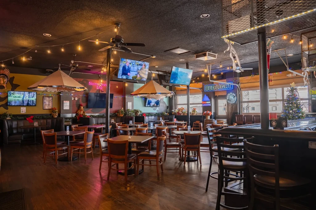 Rustic-industrial sports bar interior with TVs, booths, and string lights.