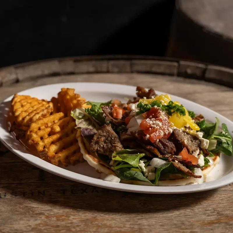 Deconstructed gyro with seasoned meat, vegetables, feta, sauce, and waffle fries.