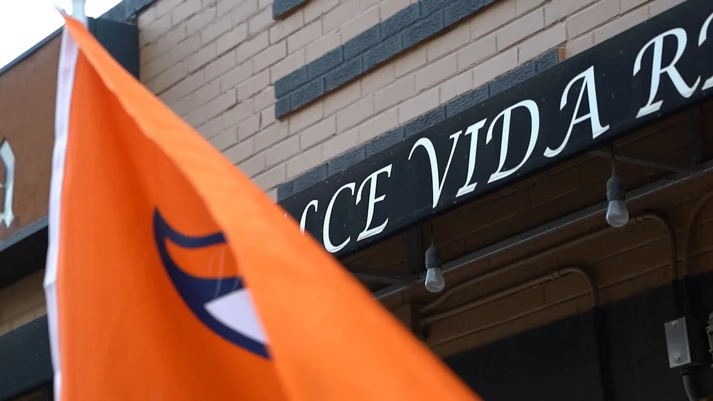 Orange flag partially obscures a sign reading "CCE VIDA R..." on a brick wall.