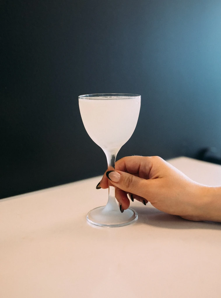 Frosty pale cocktail in coupe glass held by a hand.