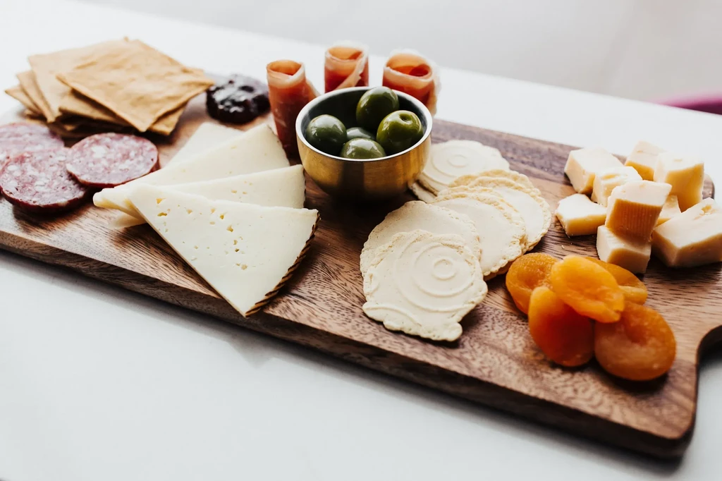 Charcuterie board featuring cheeses, cured meats, crackers, olives, and apricots.