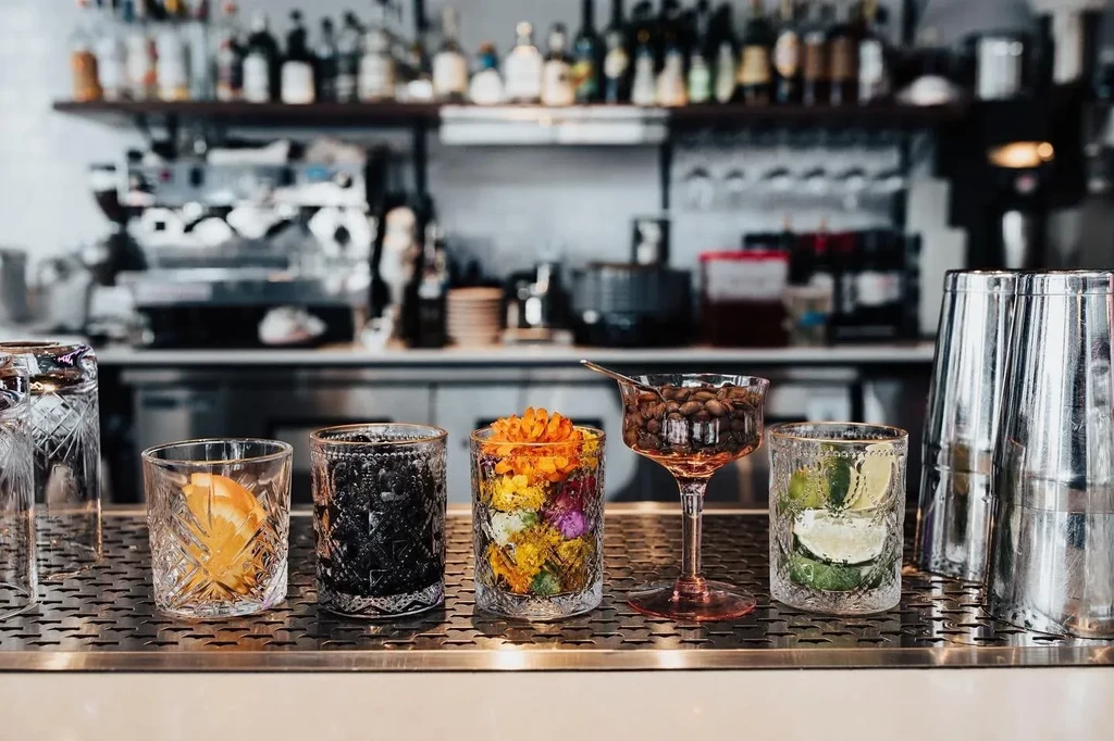 Close-up: assorted glasses, shakers, and cocktail ingredients on a bar.