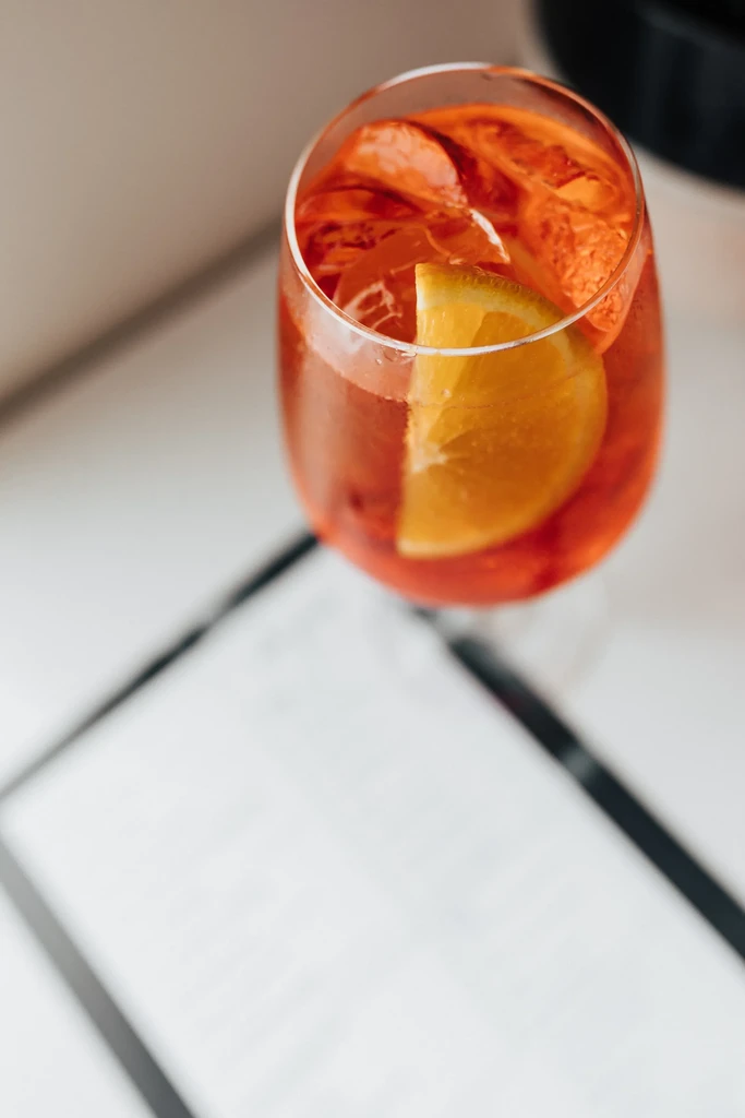 Orange-red cocktail with orange slices and ice in a stemless glass.
