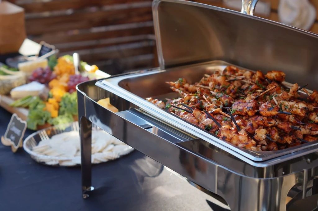 Grilled meat and vegetable skewers in a chafer dish at a buffet.