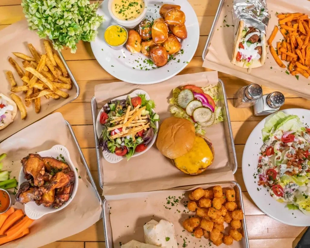 Variety of comfort foods like burgers, fries, and wings on a wooden table.