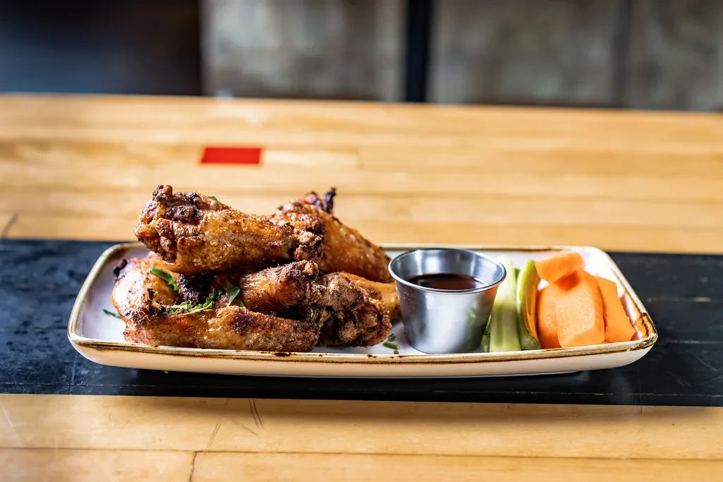 Crispy chicken wings, dipping sauce, and vegetables on a wooden table.